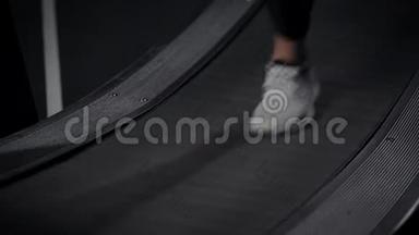 女运动员的脚在健身房的跑步机上移动，穿着运动鞋的鞋，可以看到细节